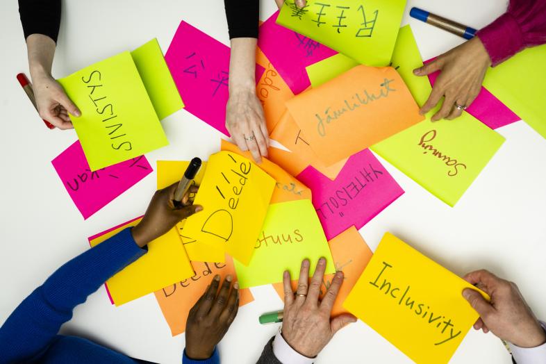 Multiple hand spreading post-it notes with terms related to community and inclusivity written on them.