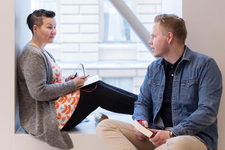 Kaksi opiskelijaa keskustelee ikkunan ääressä.