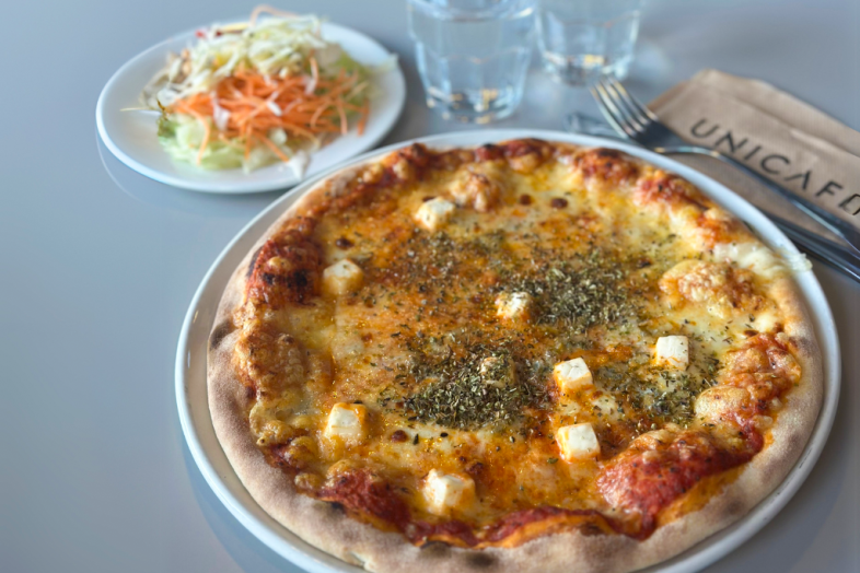 Pizza on a plate, in the back, a plate of salad, two glasses of water and a fork.
