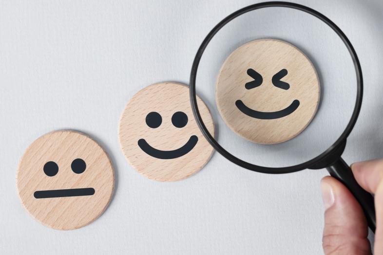 Three smiling blocks of wood and a magnifying glass showing the widest smiling block of wood.