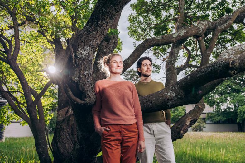 Two people stand in front of a tree.