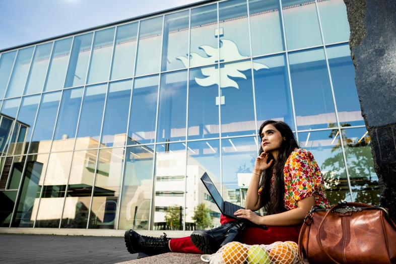 A person working under a tree in fron of the Physicum building in Kumpula.