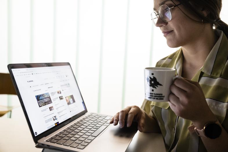henkilö kannettavan tietokoneen äärellä muki kädessä
