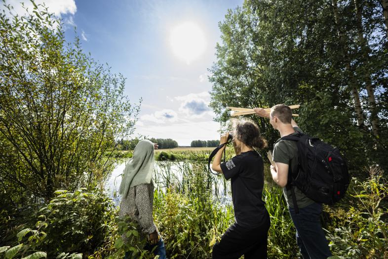 Kolme ihmistä tähyää lammelle.